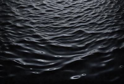The primary subject of the image is a large body of water, which appears to be a black ocean. The setting is a vast expanse of water, with no visible land or other objects. The visual style is a black and white photo, which adds a sense of depth and contrast to the scene. The colors and mood of the image are predominantly dark and moody, with the black ocean and the lack of any other objects or colors creating a sense of vastness and emptiness.
