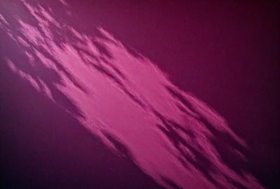 The primary subject of the image is a cloudy sky with a pink hue. The setting is a dark, cloudy sky, and the visual style appears to be a photo. The dominant colors are pink and purple, creating a moody and atmospheric scene.