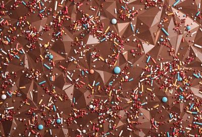 The primary subject of the image is a close-up of a chocolate cake with a pattern of candy pieces on top. The cake is decorated with a variety of candy pieces, including M&M's, which are scattered across the surface. The setting is a close-up of the cake, showcasing the intricate details of the candy pieces. The visual style is a close-up photo of the cake, highlighting the candy decorations. The colors and mood of the image are predominantly brown and warm, with the candy pieces adding a touch of color and playfulness to the scene.