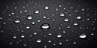 The primary subject of the image is a close-up of a raindrop on a black surface. The setting is a dark background, and the visual style is a photo. The dominant colors are black and white, with the raindrop being the only color visible. The overall atmosphere is calm and serene.