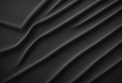 The primary subject of the image is a close-up of a black surface, possibly a piece of fabric or a wall. The setting appears to be a dark room, with the black surface being the main focus of the image. The visual style is a close-up, which emphasizes the details of the black surface. The colors and mood of the image are predominantly dark, creating a moody and mysterious atmosphere.