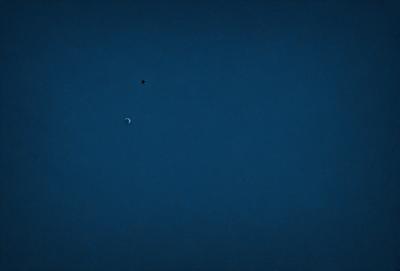 The primary subject of the image is a small moon, which is located in the middle of the scene. The setting is a dark blue sky, which creates a contrasting backdrop for the moon. The visual style of the image is a photo, capturing the moon in its natural environment. The colors and mood of the image are predominantly dark and moody, with the blue sky and the moon being the main focus.