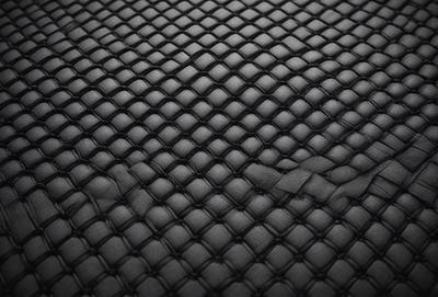 The primary subject of the image is a close-up of a black leather material. The setting is a black background, which creates a striking contrast with the leather material. The visual style is a close-up of the leather material, showcasing its texture and pattern. The colors and mood of the image are predominantly black, giving it a sleek and modern appearance.