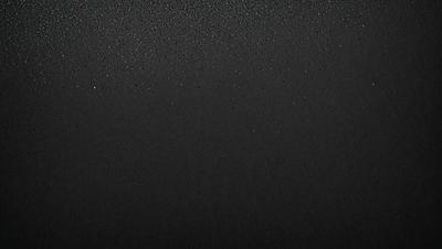 The primary subject of the image is a black background with a few white specks. The setting is a dark room, and the visual style is a black and white photo. The colors and mood of the image are predominantly dark and moody, with the white specks adding a touch of contrast.