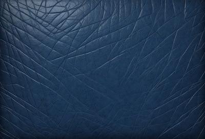 The primary subject of the image is a close-up of a blue leather material, possibly a book cover or a piece of furniture. The setting is a dark room, and the visual style appears to be a photo. The dominant colors are blue and black, creating a moody atmosphere.