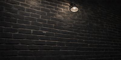 The primary subject of the image is a light fixture mounted on a brick wall. The light is shining brightly, illuminating the brick wall and creating a contrast between the light and the darker brick surface. The setting is a brick wall, which serves as the backdrop for the light fixture. The visual style of the image is a close-up of the light fixture, emphasizing its details and creating a sense of depth. The colors and mood of the image are predominantly dark, with the light fixture being the main source of brightness and contrast.