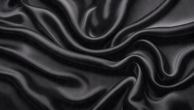 The primary subject of the image is a close-up of a black fabric, possibly a piece of clothing or a curtain. The setting is a dark background, which emphasizes the fabric's texture and pattern. The visual style is a close-up, which highlights the fabric's details. The colors and mood of the image are predominantly dark, with the black fabric being the main focus.