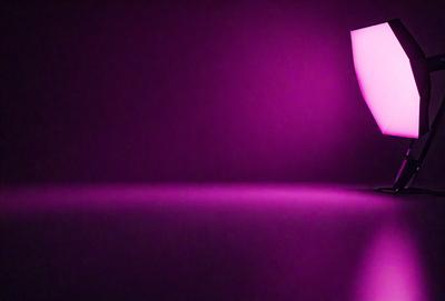 The primary subject of the image is a pink light source, which appears to be a light bulb or a purple light. The light source is located on a purple surface, which could be a table or a wall. The visual style of the image is a close-up of the light source, emphasizing its color and texture. The colors and mood of the image are predominantly pink and purple, creating a warm and inviting atmosphere.