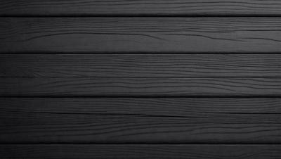 The primary subject of the image is a wooden wall. The setting is a black background, which creates a striking contrast with the wooden surface. The visual style is a close-up of the wooden wall, showcasing its texture and details. The colors and mood of the image are predominantly black, giving it a sleek and modern appearance.