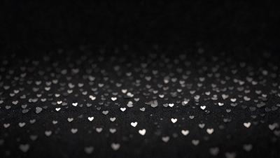 The primary subject of the image is a pattern of hearts, which are scattered across a black background. The hearts are shining and appear to be made of glitter or sequins. The setting is a dark background, which emphasizes the hearts' shine and creates a visually striking contrast. The visual style is a combination of digital art and illustration, as the hearts are carefully placed and the overall composition is well-executed. The colors and mood of the image are predominantly black and white, with the hearts adding a touch of brightness and playfulness to the scene.