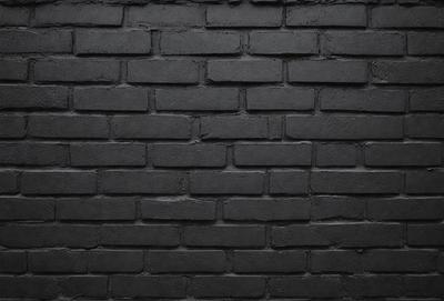 The primary subject of the image is a black brick wall. The setting is a brick wall, and the visual style is a photo. The dominant colors are black and grey, creating a moody atmosphere.