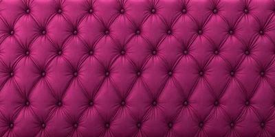 The primary subject of the image is a purple velvet couch with a patterned design. The setting is a room with a pink background, which adds to the overall atmosphere. The visual style is a close-up of the couch, showcasing its texture and pattern. The colors and mood of the image are predominantly pink, creating a warm and inviting ambiance.