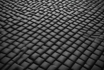 The primary subject of the image is a black fabric with a pattern of interlocking squares. The setting is a black background, and the visual style appears to be a close-up of the fabric. The colors and mood of the image are predominantly dark and moody, with the black fabric creating a sense of depth and intricacy.