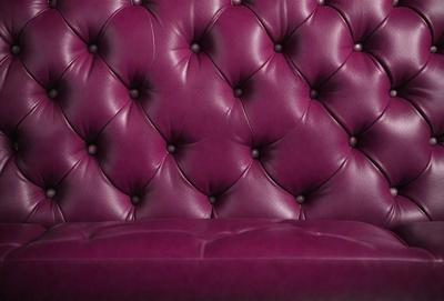 The primary subject of the image is a purple leather couch. The setting is a room with a purple couch as the main focus. The visual style is a photo, and the colors and mood are predominantly purple, creating a cozy and inviting atmosphere.
