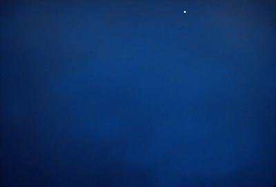 The primary subject of the image is the sky, which is a deep shade of blue. The setting is a cloudy night, with the sky being the main focus of the image. The visual style is a photo, capturing the beauty of the night sky. The colors and mood of the image are serene and peaceful, with the blue sky and clouds creating a calming atmosphere.