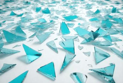 The primary subject of the image is a collection of broken blue glass pieces scattered across a white surface. The setting is an indoor environment, possibly a workshop or a place where glass is being repaired or created. The visual style is a mix of photo and digital art, as the broken glass pieces are arranged in a visually appealing manner. The colors and mood of the image are predominantly blue, with the white surface providing a clean and neutral backdrop.