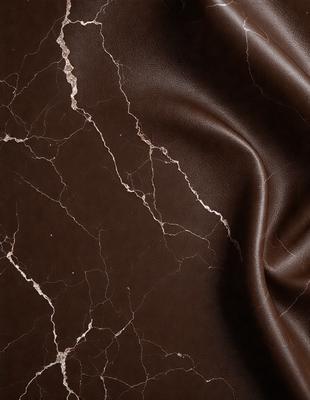 The primary subject of the image is a piece of leather with a marbled texture. The setting is a close-up of the leather, showcasing its unique pattern. The visual style is a realistic representation of the leather, capturing its natural texture and appearance. The colors and mood of the image are predominantly brown, giving it a warm and earthy feel.