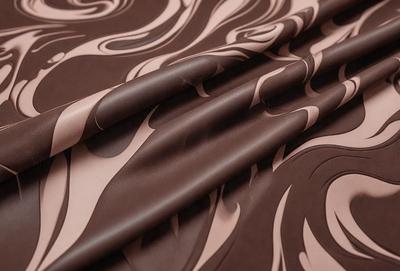 The primary subject of the image is a roll of brown fabric with a pattern of swirls and waves. The setting is a table, and the visual style appears to be a combination of a photo and a drawing. The colors and mood of the image are warm and inviting, with the brown fabric and swirling patterns creating a sense of depth and texture.