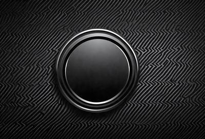 The primary subject of the image is a black button with a circular shape. The button is located on a black background, which gives it a contrasting appearance. The visual style of the image is a close-up of the button, emphasizing its shape and texture. The colors and mood of the image are predominantly black, creating a sleek and modern look.