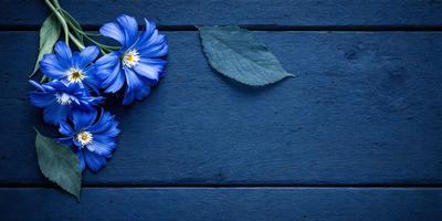 The primary subject of the image is a blue flower, which is placed on a wooden surface. The setting is a wooden table, and the visual style is a photo. The dominant colors in the image are blue and green, creating a calm and serene atmosphere.