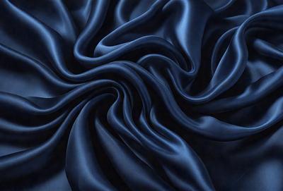 The primary subject of the image is a close-up of a blue fabric, possibly a piece of silk or velvet. The setting is a dark background, which emphasizes the richness of the blue fabric. The visual style appears to be a close-up of the fabric, showcasing its texture and details. The colors and mood of the image are predominantly blue, creating a sense of calmness and sophistication.