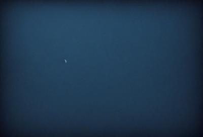 The primary subject of the image is the moon, which is visible in the sky. The setting is a dark, cloudless night with a clear view of the moon. The visual style is a photo, capturing the beauty of the moon in the night sky. The colors and mood of the image are predominantly dark, with the moon being the main source of light, creating a serene and peaceful atmosphere.
