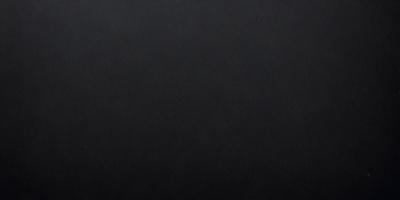 The primary subject of the image is a black leather surface. The setting is a dark room, and the visual style is a close-up of the leather surface. The colors and mood of the image are predominantly dark and moody, with the black leather being the main focus.