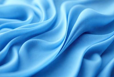 The primary subject of the image is a blue fabric, possibly a piece of silk, with a flowing and swirling pattern. The setting is a blue background, which complements the blue fabric. The visual style is a close-up of the fabric, showcasing its texture and pattern. The colors and mood of the image are predominantly blue, creating a calm and serene atmosphere.