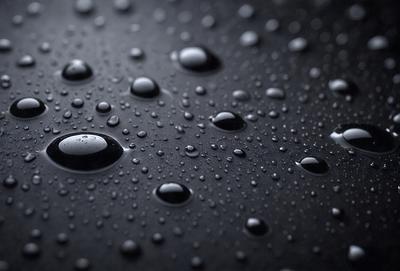 The primary subject of the image is a close-up of a raindrop on a black surface. The setting is a dark background, and the visual style appears to be a photo. The dominant colors are black and white, with the raindrop being the only color visible. The overall atmosphere is moody and dramatic.