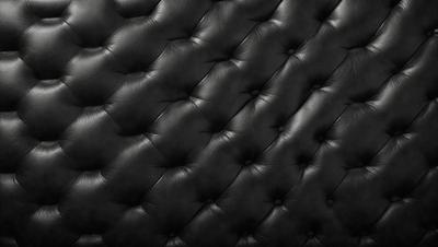 The primary subject of the image is a black leather couch with a patterned design. The setting is a room with a black background, which creates a contrast with the couch. The visual style is a close-up of the couch, showcasing its texture and pattern. The colors and mood of the image are predominantly black, giving it a sleek and modern appearance.