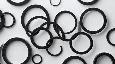 The primary subject of the image is a collection of black circles, which are arranged in various sizes and shapes. The setting is a white background, which provides a clean and uncluttered environment for the circles. The visual style of the image is a close-up of the circles, showcasing their details and textures. The dominant colors in the image are black and white, creating a bold and striking contrast. The overall atmosphere of the image is one of simplicity and elegance, with the black circles serving as the focal point.