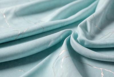 The primary subject of the image is a blue sheet of fabric. The setting is a bed, and the visual style is a close-up of the fabric. The colors and mood of the image are predominantly blue, creating a calm and soothing atmosphere.