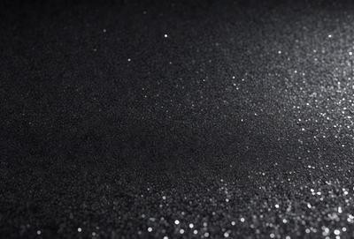 The primary subject of the image is a close-up of a black surface with a pattern of glittering specks. The setting is a dark background, and the visual style appears to be a photo or a digital artwork. The colors in the image are predominantly black, with the glittering specks adding a touch of brightness and visual interest. The overall atmosphere of the image is somewhat mysterious and intriguing, as the viewer is drawn to the captivating pattern of the glittering specks.