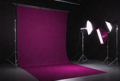 The primary subject of the image is a pink background, which is likely a backdrop for a photo shoot. The setting is a dark room, with a purple cloth covering the floor. The visual style appears to be a photo, as the background is clearly visible and the overall atmosphere is dark and moody. The colors and mood of the image are dominated by the pink and purple hues, creating a unique and artistic atmosphere.