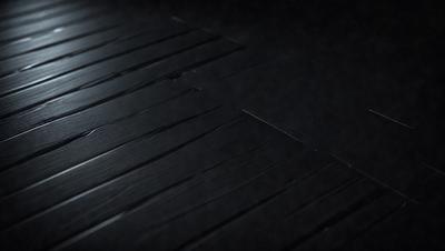 The primary subject of the image is a wooden floor with a black surface. The setting is a dark room, and the visual style appears to be a photo. The colors and mood of the image are predominantly dark, with a sense of mystery or intrigue.