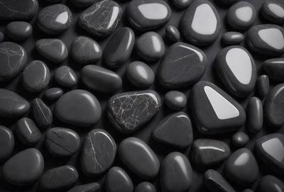 The primary subject of the image is a collection of black rocks. The setting is a dark background, which contrasts with the black rocks. The visual style is a close-up of the rocks, showcasing their unique textures and patterns. The colors and mood of the image are predominantly dark and moody, with the black rocks serving as the focal point.