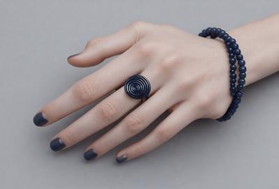 The primary subject of the image is a woman's hand wearing a ring. The setting is a gray background, which provides a clean and minimalist look. The visual style is a close-up of the woman's hand, showcasing the ring and the surrounding skin. The colors in the image are predominantly gray, which contributes to the overall mood of the image.