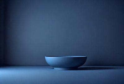The primary subject of the image is a blue bowl placed on a blue surface. The setting appears to be a dark room, with the bowl being the main focus of the image. The visual style is a photo, and the dominant colors are blue, creating a calm and serene atmosphere.