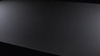 The primary subject of the image is a black background with a white surface. The setting is a dark room, and the visual style is a black and white photo. The colors and mood of the image are predominantly dark and moody, with the black background and white surface creating a stark contrast.