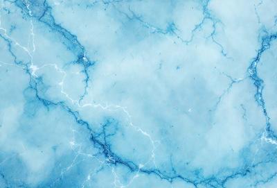 The primary subject of the image is a blue and white marble-like surface, which appears to be a wall or a countertop. The setting is a room with a blue and white color scheme. The visual style is a close-up of the marble surface, showcasing its intricate patterns and textures. The colors and mood of the image are predominantly blue and white, creating a calm and serene atmosphere.