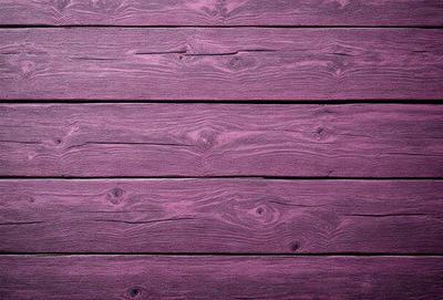 The primary subject of the image is a wooden wall with a purple color. The setting is a room with a wooden floor. The visual style is a close-up of the wooden wall, showcasing its texture and color. The dominant colors are purple and brown, creating a warm and cozy atmosphere.
