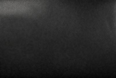 The primary subject of the image is a black leather surface. The setting is a black background, which creates a contrast with the leather. The visual style is a close-up of the leather, showcasing its texture and details. The colors and mood of the image are predominantly dark and moody, with the black leather serving as the focal point.