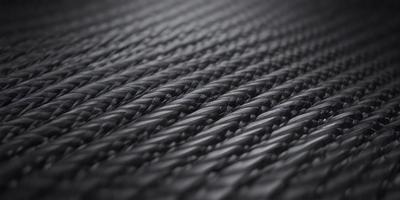 The primary subject of the image is a close-up of a black rope. The setting is a black background, which creates a striking contrast with the rope. The visual style is a black and white photo, giving the image a classic and timeless appearance. The dominant colors are black and white, and the overall atmosphere is one of simplicity and elegance.