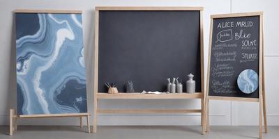 The primary subject of the image is a chalkboard with a wooden frame. The setting is a table with various items on it, including a vase, a bowl, and a bottle. The visual style is a photo, and the colors and mood are predominantly neutral, with a focus on the wooden frame and the chalkboard.