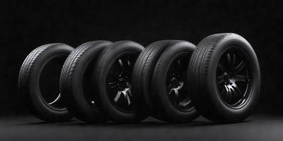 The primary subject of the image is a row of tires, which are the main objects in the scene. The tires are lined up next to each other, creating a visually appealing arrangement. The setting is a black background, which contrasts with the tires, making them stand out. The visual style of the image is a photo, capturing the tires in their natural environment. The colors and mood of the image are predominantly black, giving it a sleek and modern appearance.