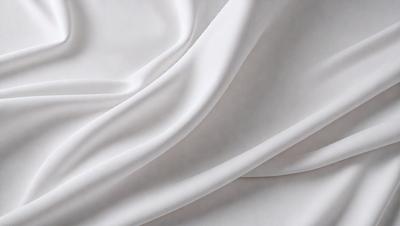 The primary subject of the image is a white sheet of fabric. The setting is a white background, which creates a clean and minimalist appearance. The visual style is a close-up of the fabric, showcasing its texture and details. The colors and mood of the image are predominantly white, giving it a calm and serene atmosphere.