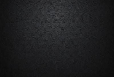 The primary subject of the image is a black and white patterned wallpaper with a black background. The setting is a room with a black wall, and the visual style is a close-up of the wallpaper. The colors and mood of the image are predominantly black, creating a bold and striking appearance.