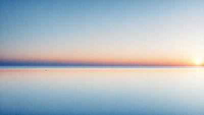 The primary subject of the image is the ocean, with a beautiful sunset in the background. The setting is a vast expanse of water, and the visual style is a photo. The colors and mood of the image are serene and calming, with the warm hues of the sunset creating a peaceful atmosphere.
