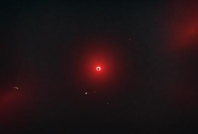 The primary subject of the image is a red circle, which appears to be a planet or a celestial object. The setting is a dark, starry sky, with the red circle being the main focus of the image. The visual style is a black and white photo, which adds a sense of depth and contrast to the scene. The colors and mood of the image are predominantly dark and moody, with the red circle standing out as the main point of interest.