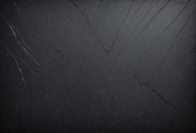 The primary subject of the image is a black countertop with a rough texture. The setting is a kitchen or a similar environment, as the countertop is a part of a kitchen counter. The visual style is a close-up of the countertop, showcasing its unique texture. The colors and mood of the image are dark and moody, with the black countertop being the dominant color.